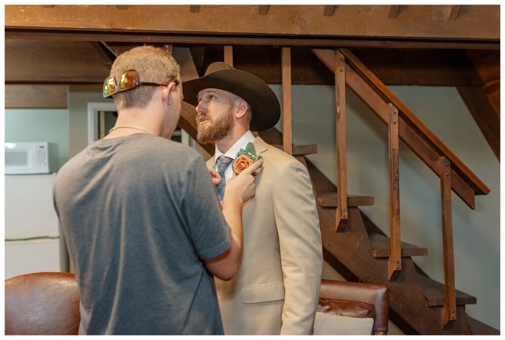 Groom getting boutonniere pinned on by groomsman