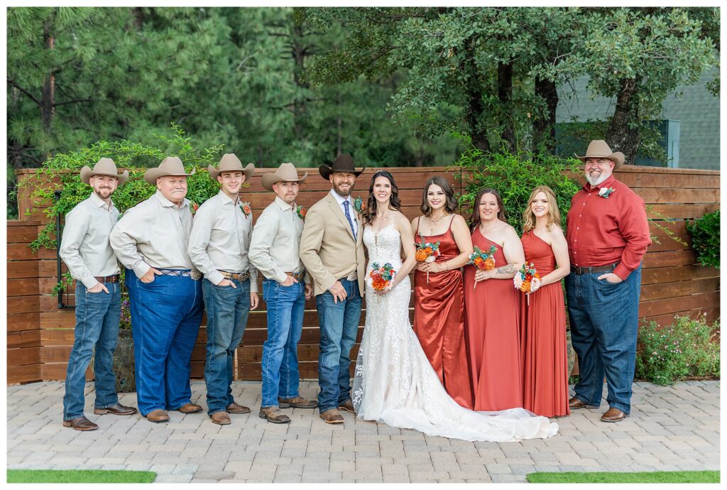 Full wedding party with groomsmen in jeans and cowboy hats, bridal part in rust. 