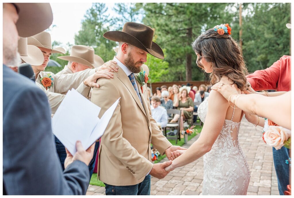 Wedding party with hands on shoulders of bride and groom during group prayer