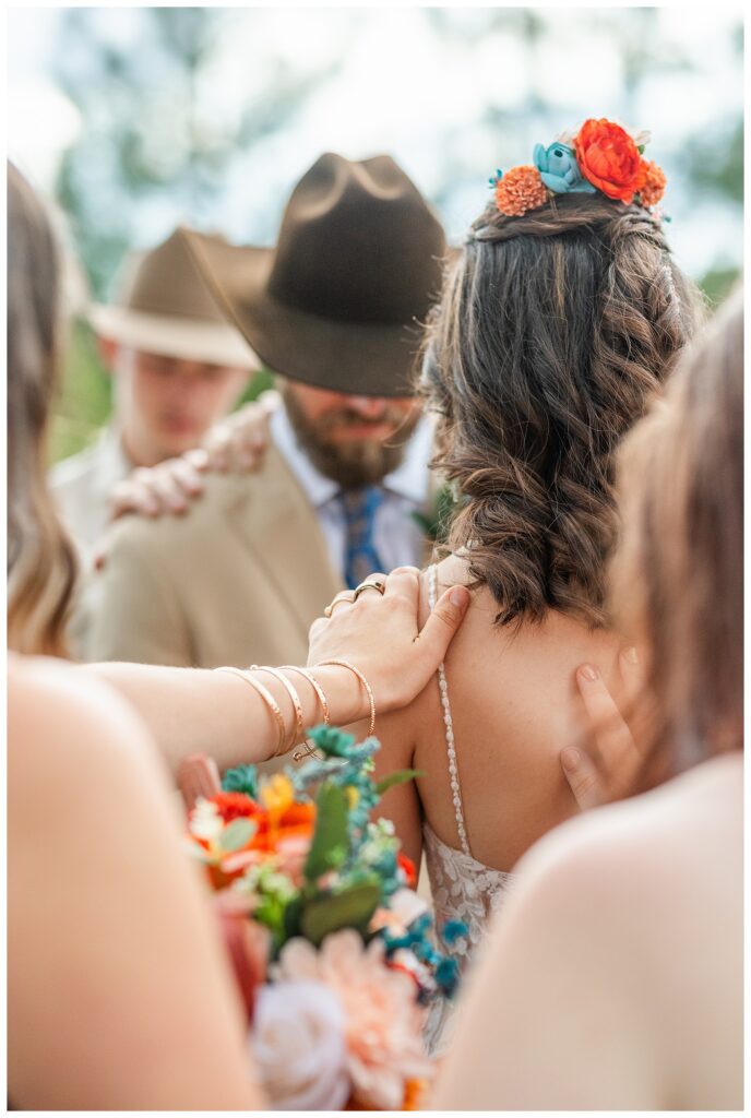 Wedding party with hands on shoulders of bride and groom during group prayer