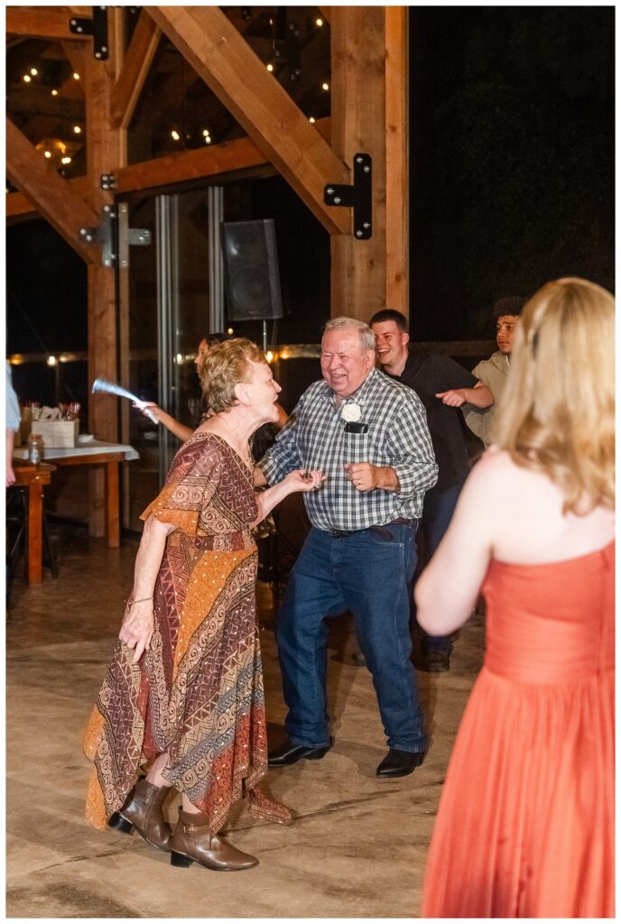 Fun wedding reception dancing under string lights inside a rustic wooden pavilion.