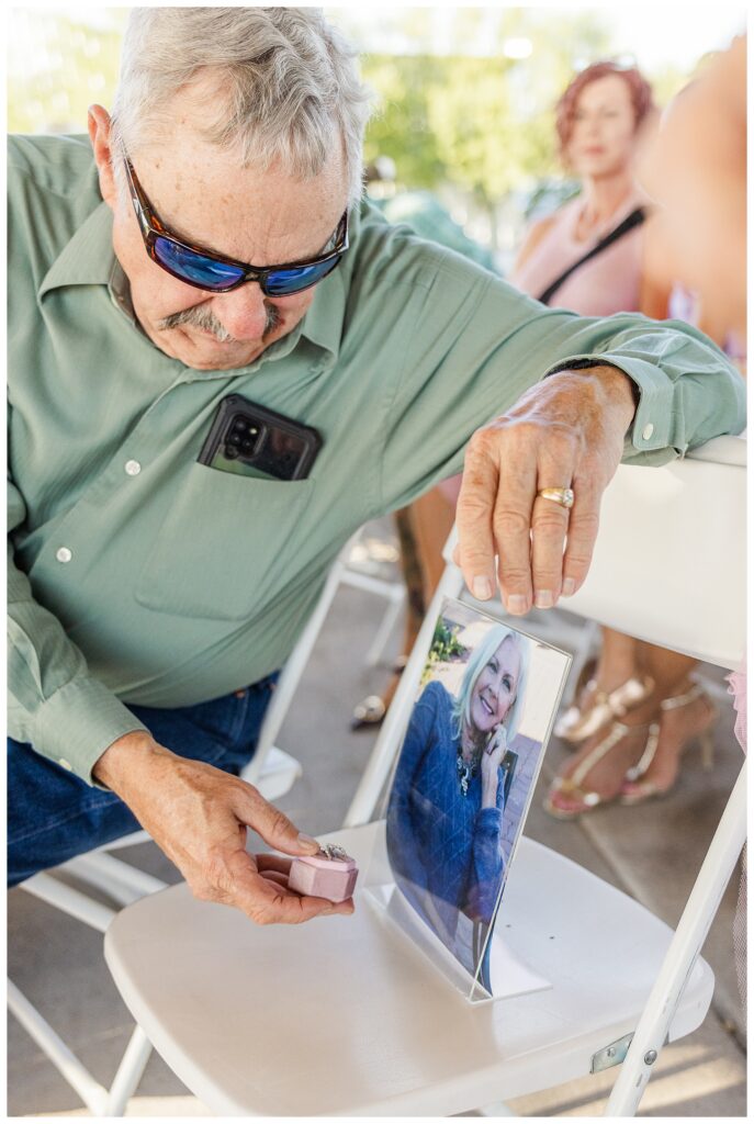 Grandpa participating in ring warming by holding rings up to recently deceased wife's photo during ring warming ceremony